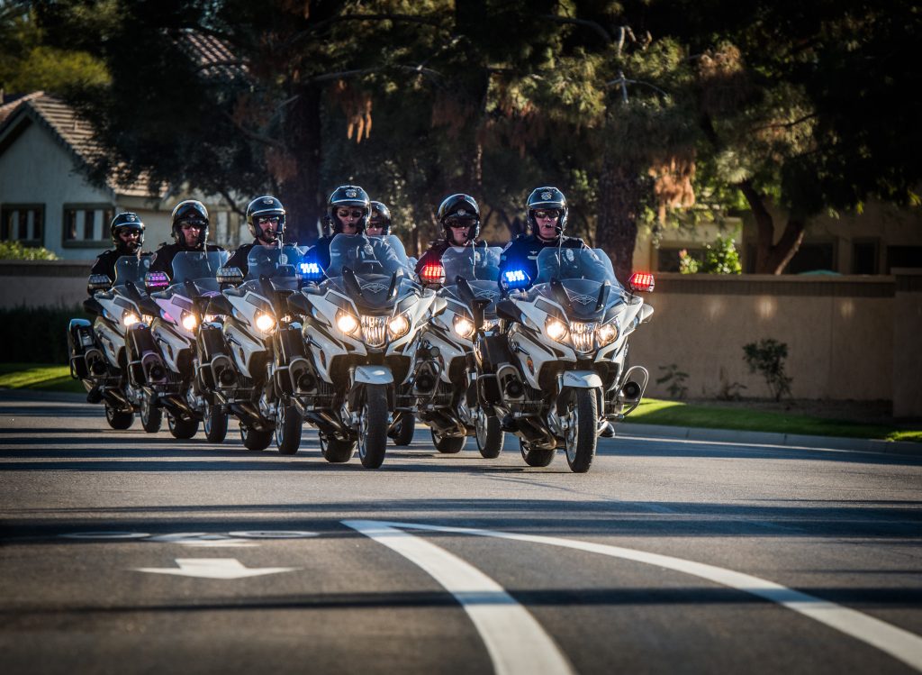 Seven motorcycle officers riding in formation on a city street.